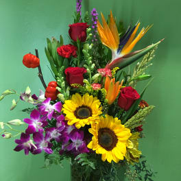 Mixed bouquet with sunflowers, roses, orchids, and bird of paradise in a glass vase
