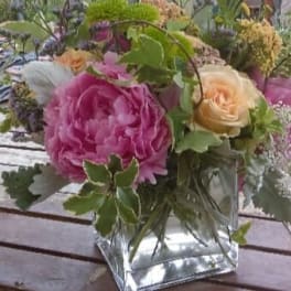 Pink and peach roses in a square glass vase with greenery