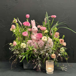 Pink floral arrangement with a rabbit figurine and a glass candle holder