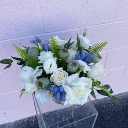 White rose bouquet with blue accents and green foliage in a clear vase
