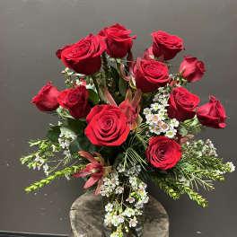 Red roses arranged in a clear glass vase with small white filler flowers