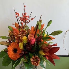 Autumn bouquet with orange gerbera daisies, lilies, and red berries in a vase