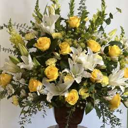 Large arrangement of yellow roses, yellow carnations, and white lilies in a brown urn vase