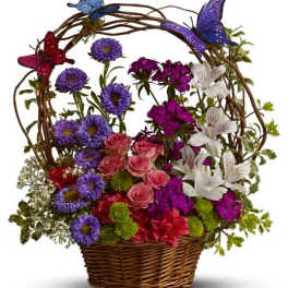 Colorful basket arrangement with mixed purple, pink, white, and green flowers and decorative butterflies on a vine arch