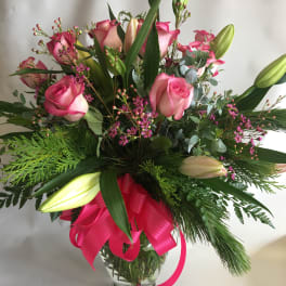 Pink roses and lilies in a glass vase with a bright ribbon
