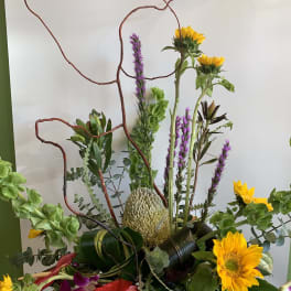 Tall floral arrangement with sunflowers, orchids, and a red anthurium