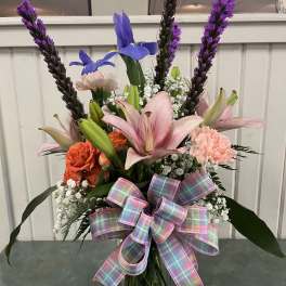 Mixed bouquet with pink lilies, orange roses, and purple spikes in a glass vase