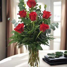 Red roses arranged in a clear glass vase with greenery