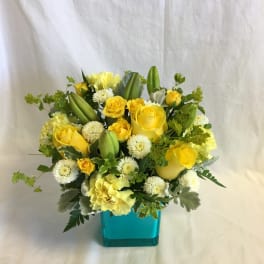 Yellow roses and white pom flowers in a turquoise vase