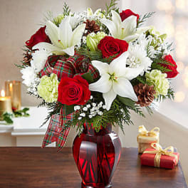 Red roses and white lilies in a red glass vase with plaid ribbon