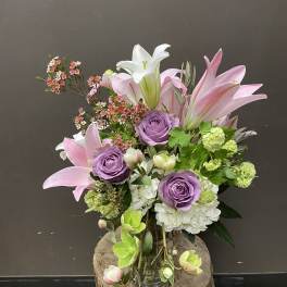 Bouquet of pink lilies, lavender roses, and white hydrangea in a glass vase