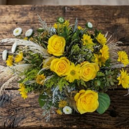 Low arrangement of yellow roses and daisies with white accents on a rustic wooden table