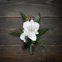White orchid boutonniere with black ribbon and gold wire accents on a dark wood surface