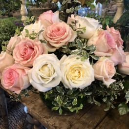 Low arrangement of pink and white roses with variegated foliage in a glass bowl vase