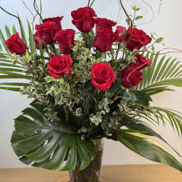Tall arrangement of red roses with large tropical leaves in a clear glass vase