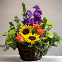 Basket arrangement with sunflowers, orange roses, and purple blooms