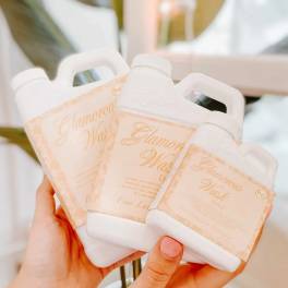 Hands holding three white bottles with peach labels.