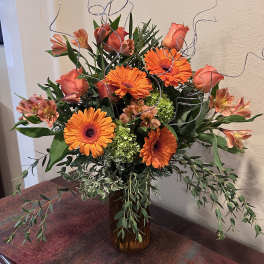 Orange gerbera daisies and roses in a glass vase