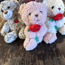 Three plush teddy bears with ribbon roses sit on a table.