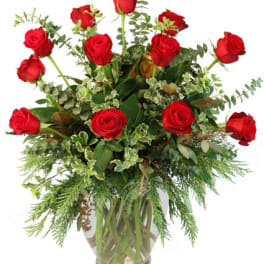 Tall arrangement of long-stem red roses with assorted foliage in a clear glass vase.