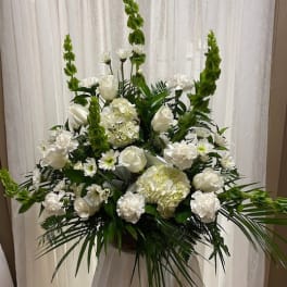 Tall white floral arrangement with roses, hydrangeas, and green spikes