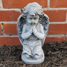 Small praying angel statue in front of a brick wall