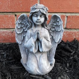 Stone angel statue kneeling with folded hands against a brick wall