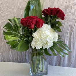 Red roses and white hydrangea in a clear glass vase with tropical leaves