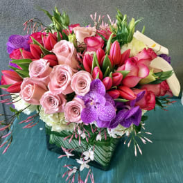Bouquet of pink roses, red tulips, and purple orchids in a glass vase