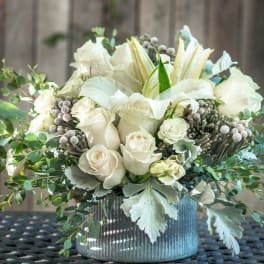 White roses and lilies arranged in a ribbed silver vase