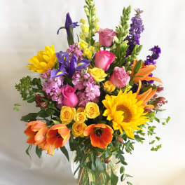Colorful mixed bouquet in a clear glass vase with sunflowers, roses, tulips, and irises