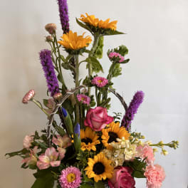 Basket arrangement with sunflowers, pink roses, and purple spikes
