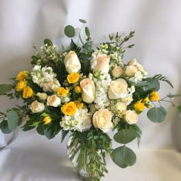 Cream and yellow roses in a clear glass vase with greenery