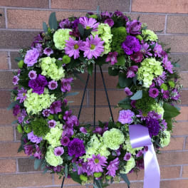 Purple and green floral wreath on a stand with a lavender ribbon