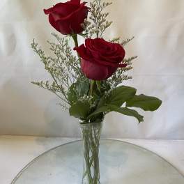 Two red roses in a clear glass vase with airy filler