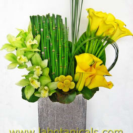 Yellow calla lilies and green orchids in a tall vase arrangement