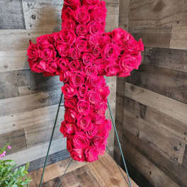 Standing cross of hot pink roses on a metal easel against a wood wall.