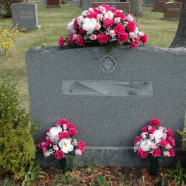 Pink and white floral arrangements on a gravestone in a cemetery