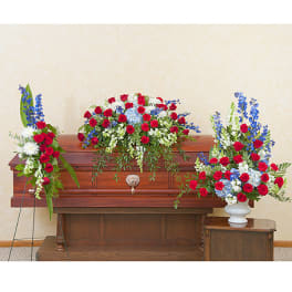 Three red, white, and blue floral funeral arrangements around a casket