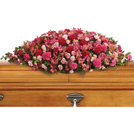Pink and red floral casket spray on a wooden coffin