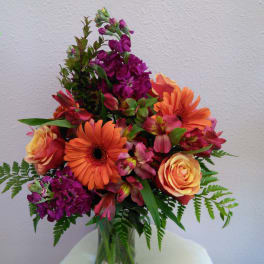 Mixed bouquet of orange, pink, and purple flowers in a glass vase