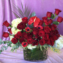 Red rose arrangement in a glass vase with white blooms and tropical accents