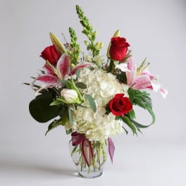 Red roses and pink lilies arranged with white hydrangea in a glass vase