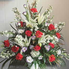 Large mixed floral arrangement with red roses, white lilies, and white blossoms in a vase
