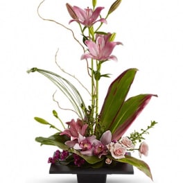 Tall floral arrangement with pink lilies and orchids in a black container