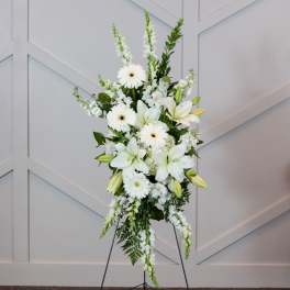 White floral standing spray on an easel with lilies and daisies