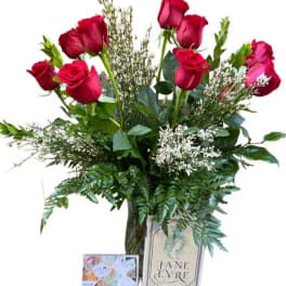 Red roses in a glass vase with greenery and a greeting card