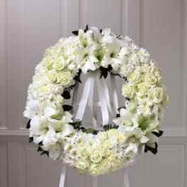 White floral wreath on a stand with roses and lilies