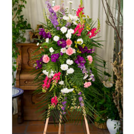 Tall standing spray of pink, white, and purple flowers with abundant greenery on a wooden easel
