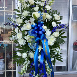 Tall white and blue funeral spray on an easel with a blue ribbon